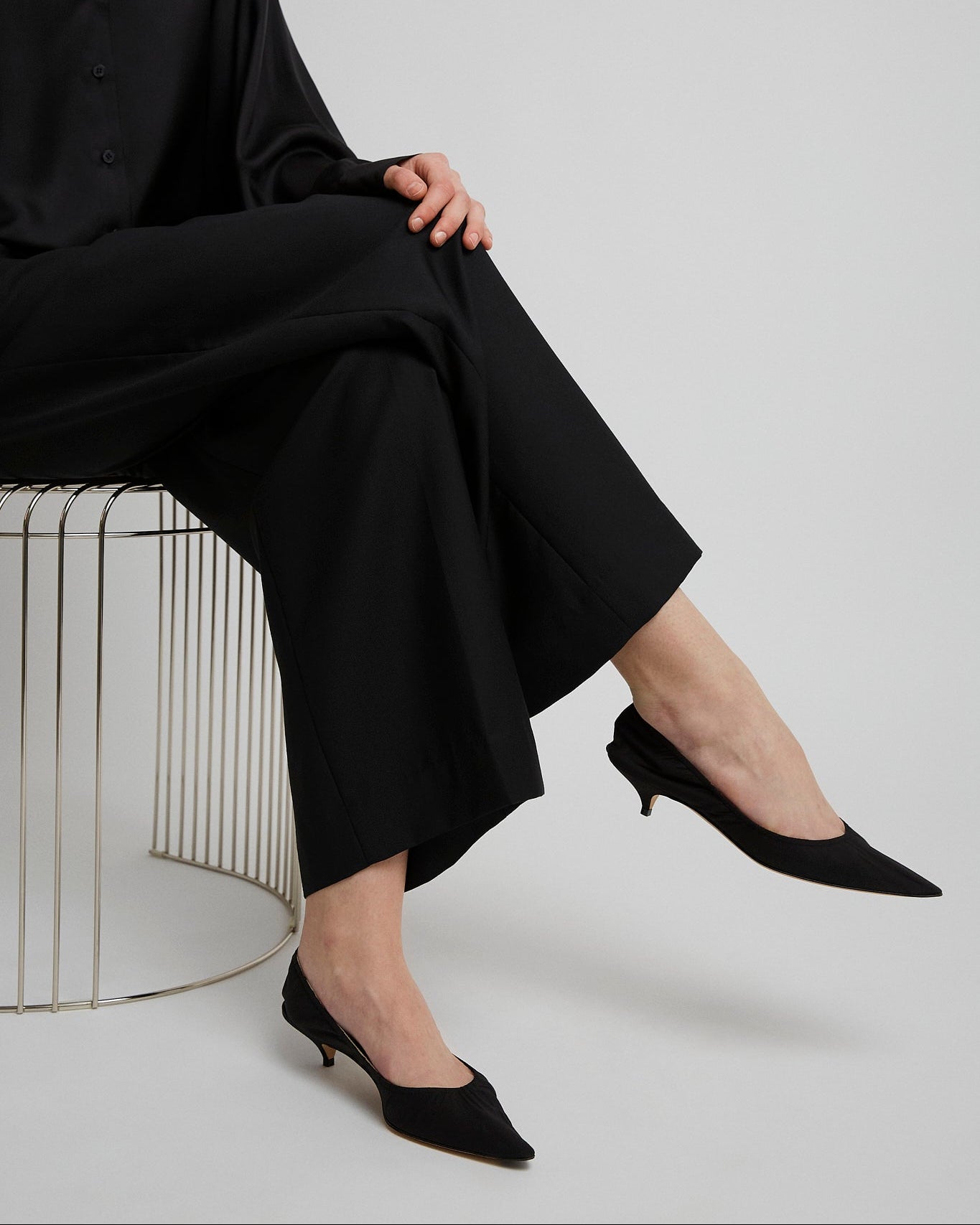 Person wearing a black outfit with wide-leg pants and black shoes on a white background