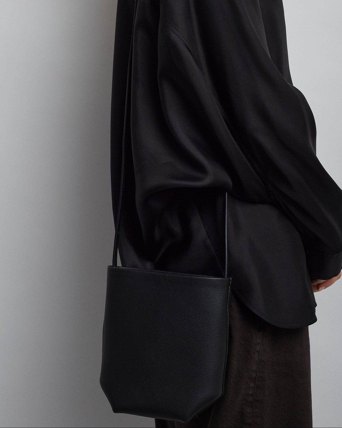 Person wearing a black coat holding a black bag against a plain background