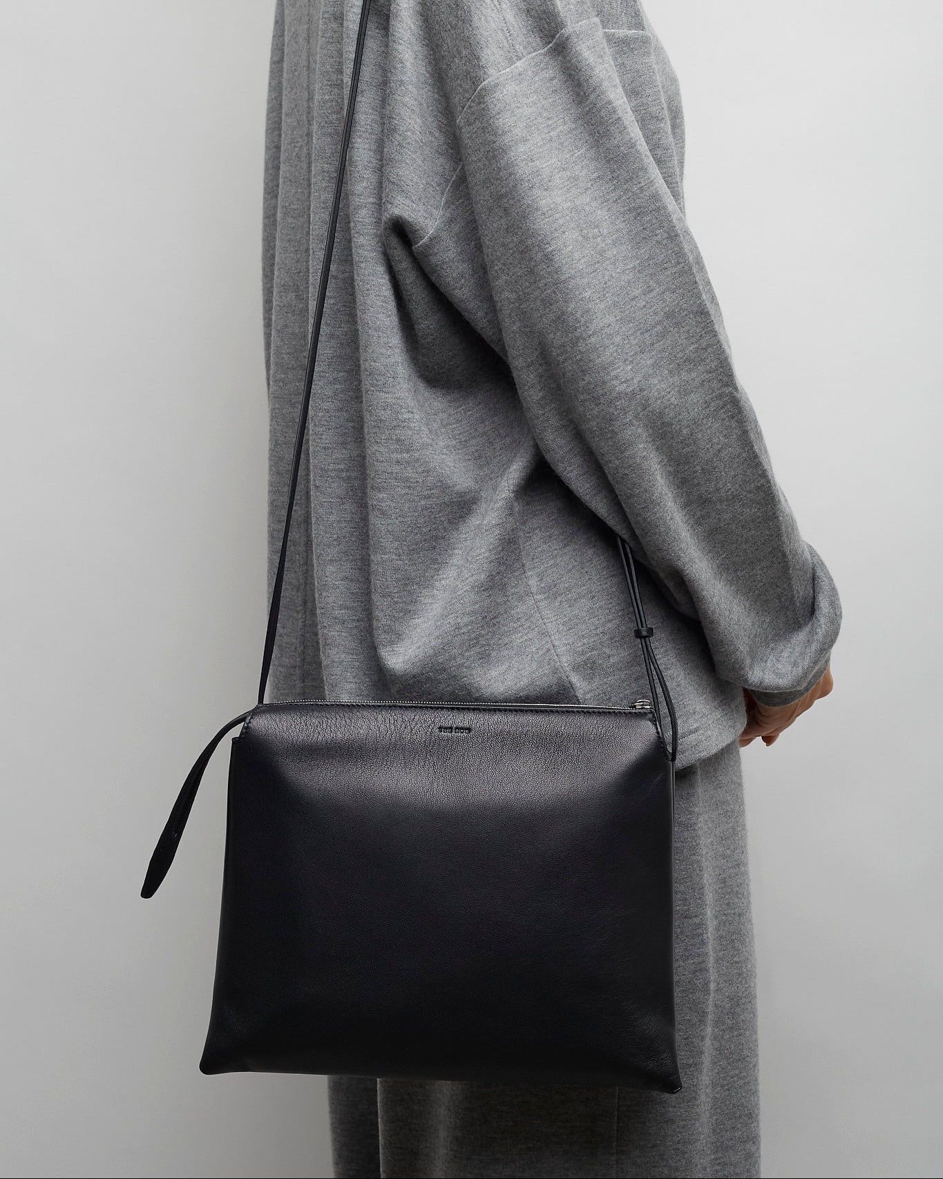Person wearing a gray coat holding a black bag against a plain background