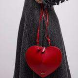 Red heart-shaped handbag held by a person wearing a gray dress against a white background