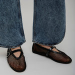 Person wearing black mesh shoes and blue jeans on a plain background