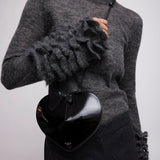 Person wearing a gray sweater with ruffled sleeves holding a black heart-shaped bag.
