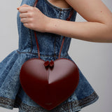 Heart-shaped handbag held by a person wearing a denim outfit on a plain background