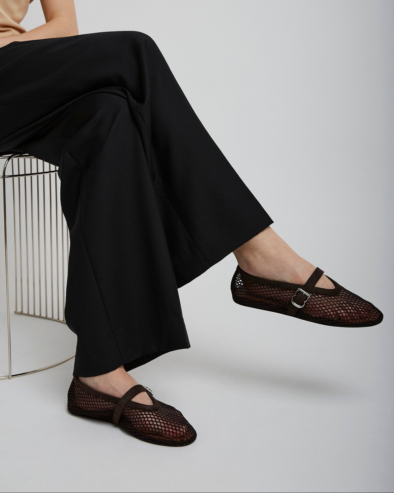 Person wearing black mesh sandals sitting on a chair with a plain background