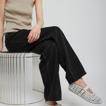 Person wearing a beige sleeveless top and black pants, sitting on a wire stool with white shoes.