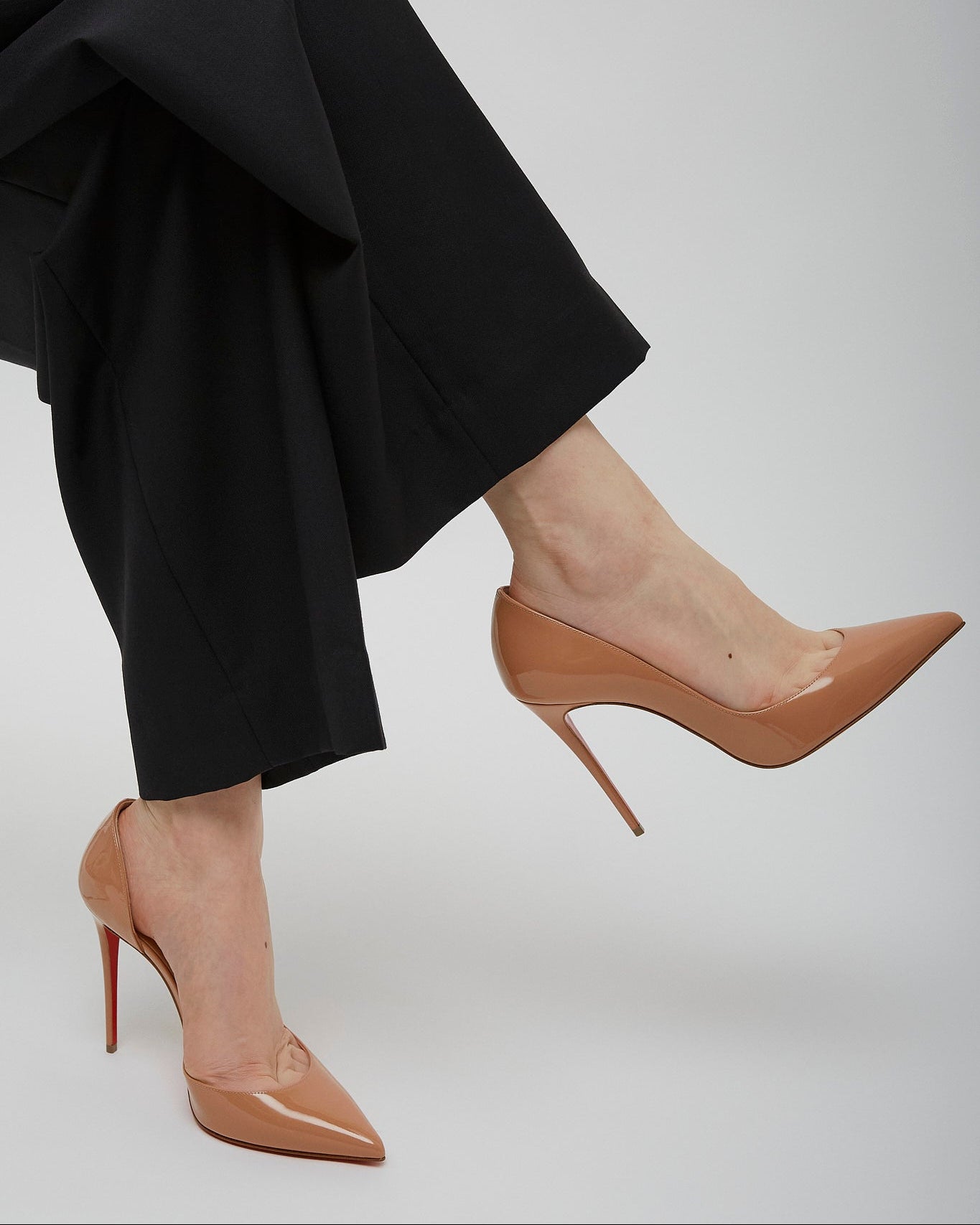 Person wearing black pants and tan high-heeled shoes on a plain background