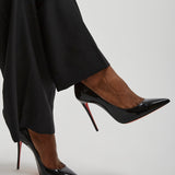 Black high-heeled shoes worn with black pants on a light gray background