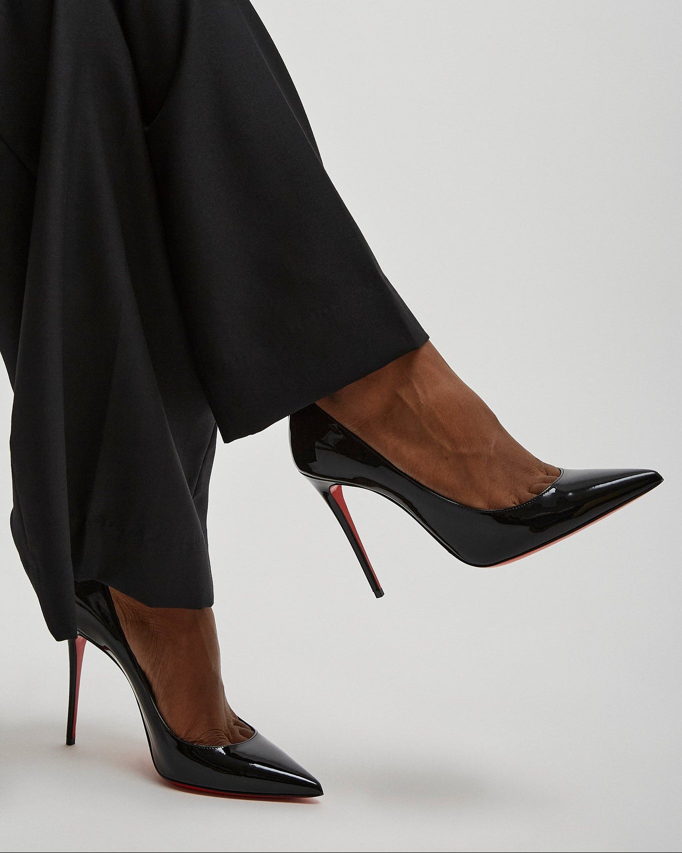 Black high-heeled shoes worn with black pants on a light gray background
