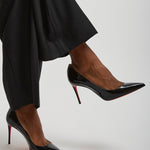 Black high-heeled shoes worn with black pants on a light gray background