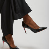 Black high-heeled shoes worn with black pants on a light gray background