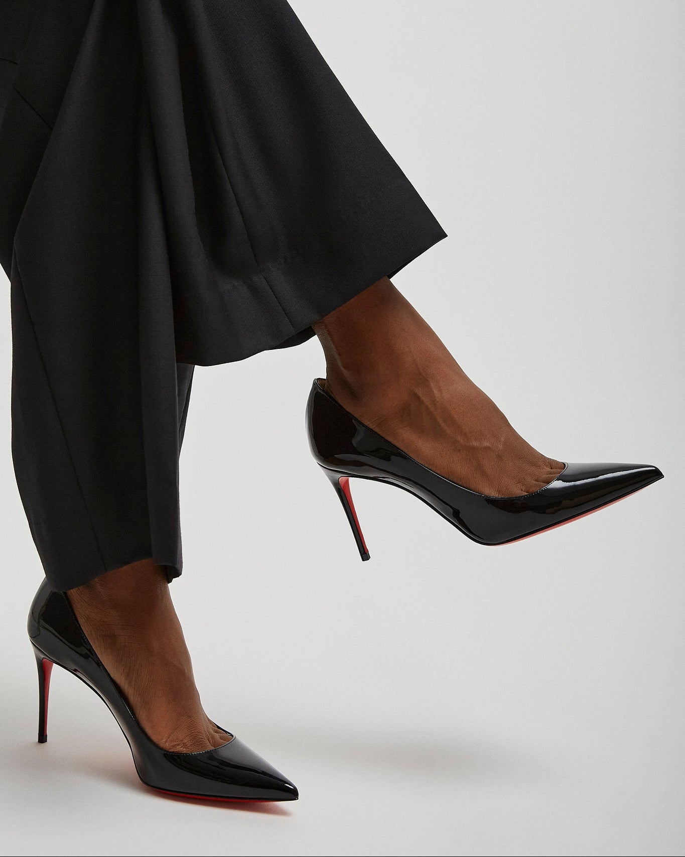 Black high-heeled shoes worn with black pants on a light gray background