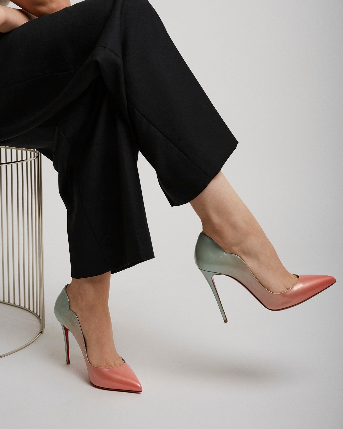 Person wearing black pants and pink high-heeled shoes on a white background