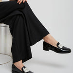 Person wearing black shoes with silver buckles sitting on a white chair.