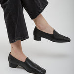 Person wearing black loafers and black jeans on a light gray background