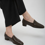 Person wearing brown leather shoes and black pants on a white background