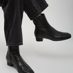 Black leather ankle boots worn with black jeans on a light gray background