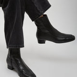 Black leather ankle boots worn with black jeans on a light gray background
