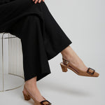 Person wearing black pants and brown shoes with a white background