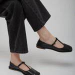 Person wearing black flat shoes and black jeans on a light gray background