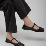 Person wearing black flat shoes and black jeans on a light gray background