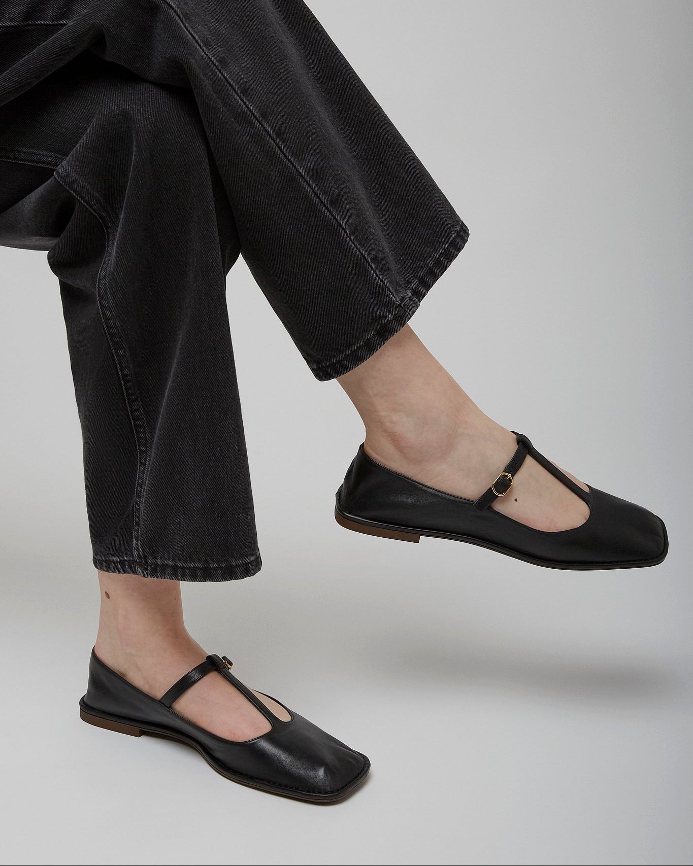 Person wearing black flat shoes and black jeans on a light gray background